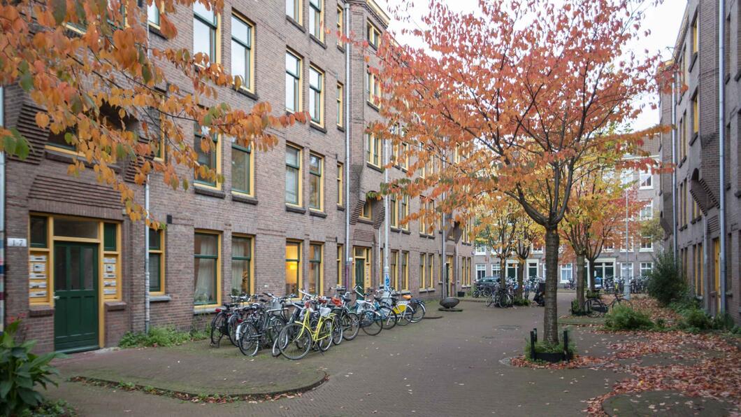 Woningen grenzend aan een pleintje met veel geparkeerde fietsen en bomen in rode herfstkleuren